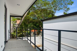 A narrow balcony with a metal railing, leading to a covered outdoor area with trees and a building in the background. - Brisas Tranquilas #1 is a private 2-bedroom, 2-bathroom retreat with a fully equipped kitchen, washer and dryer, private pool, and parking. Enjoy a peaceful and comfortable stay with everything you need for a relaxing getaway. (Playas Del Coco)