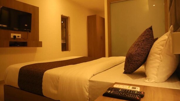 A hotel room with a bed, pillows, a remote control, and a television on the wall.