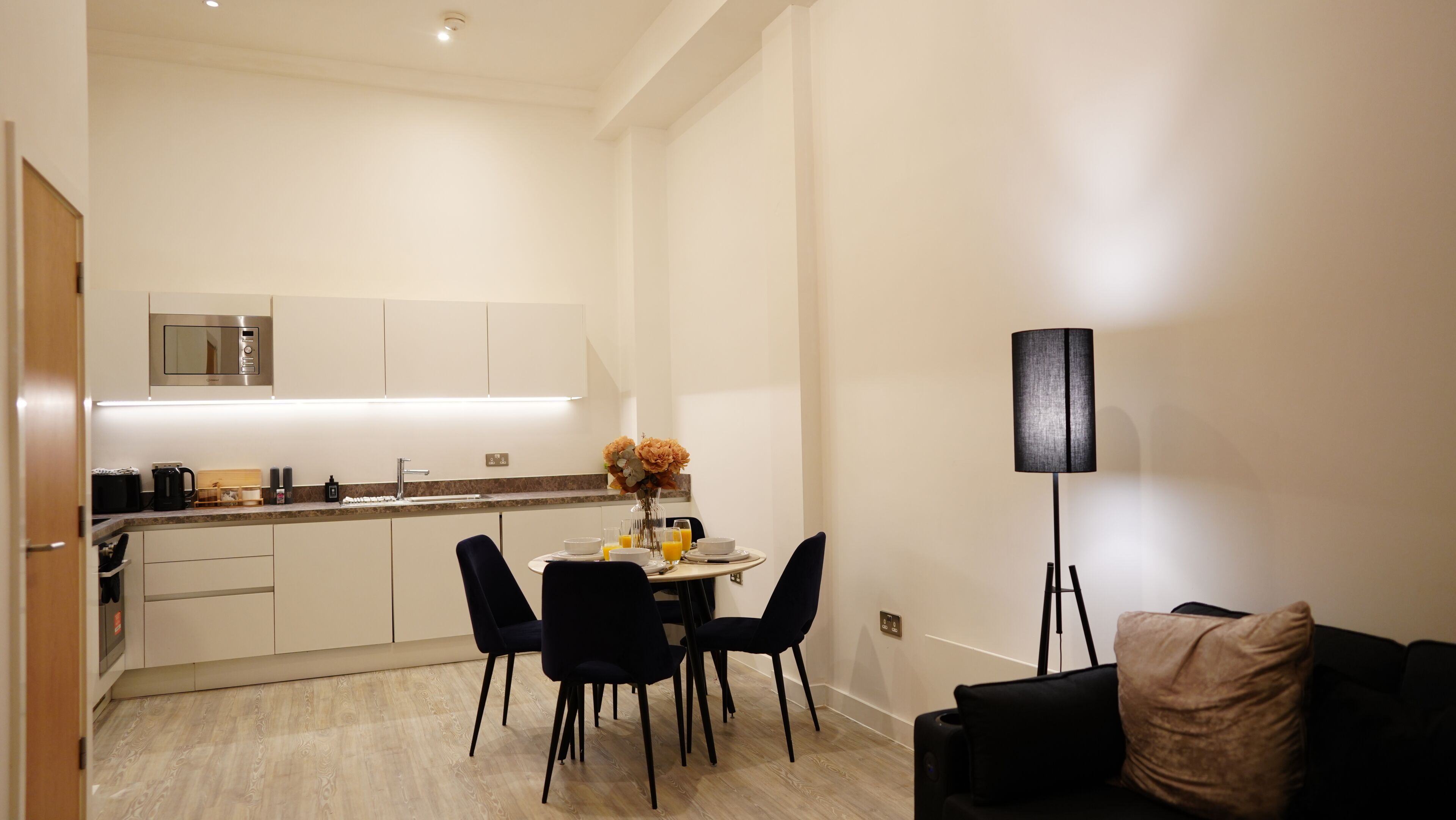 Une cuisine compacte dotée d’appareils électroménagers modernes, un coin repas avec une table ronde et des chaises, et un lampadaire.