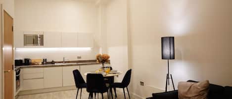 A compact kitchen with modern appliances, a dining area with a round table and chairs, and a floor lamp.