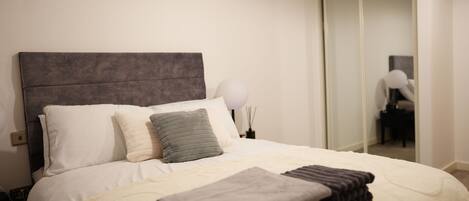 A neatly made bed with pillows and a folded blanket, a bedside lamp, and a mirror on the wall.