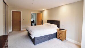 A bedroom with a bed, a bedside table, a wardrobe, and a bathroom visible through an open door. - Cefn Coed (Presteigne)