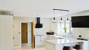 A modern kitchen with a large island, bar stools, pendant lights, and a flat-screen TV. - Cefn Coed (Presteigne)