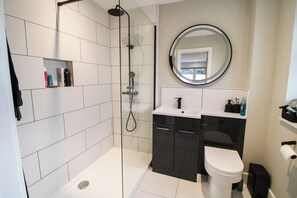 Ein modernes Badezimmer mit einer einteiligen Duschkabine, einem runden Spiegel, einer weißen Toilette und einem dunklen Waschtisch.