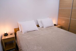 A neatly made bed with white bedding and pillows, a bedside table with a lamp, and a wooden headboard.