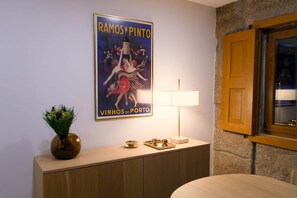 Una habitación con un cartel en la pared, una mesita de noche con lámpara y una ventana con contraventanas de madera.
