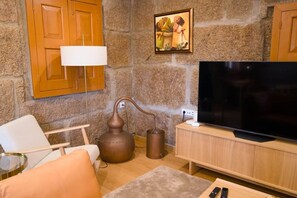 Una sala de estar con una pared de piedra, armarios de madera, un televisor, una lámpara y un sillón.