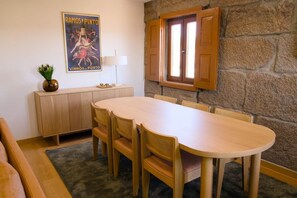 A dining area with a round wooden table and chairs, a wooden cabinet, a potted plant, and a poster on the wall.