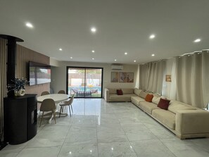 Un salon moderne comprenant un canapé, un téléviseur et un coin repas avec des chaises et une table.