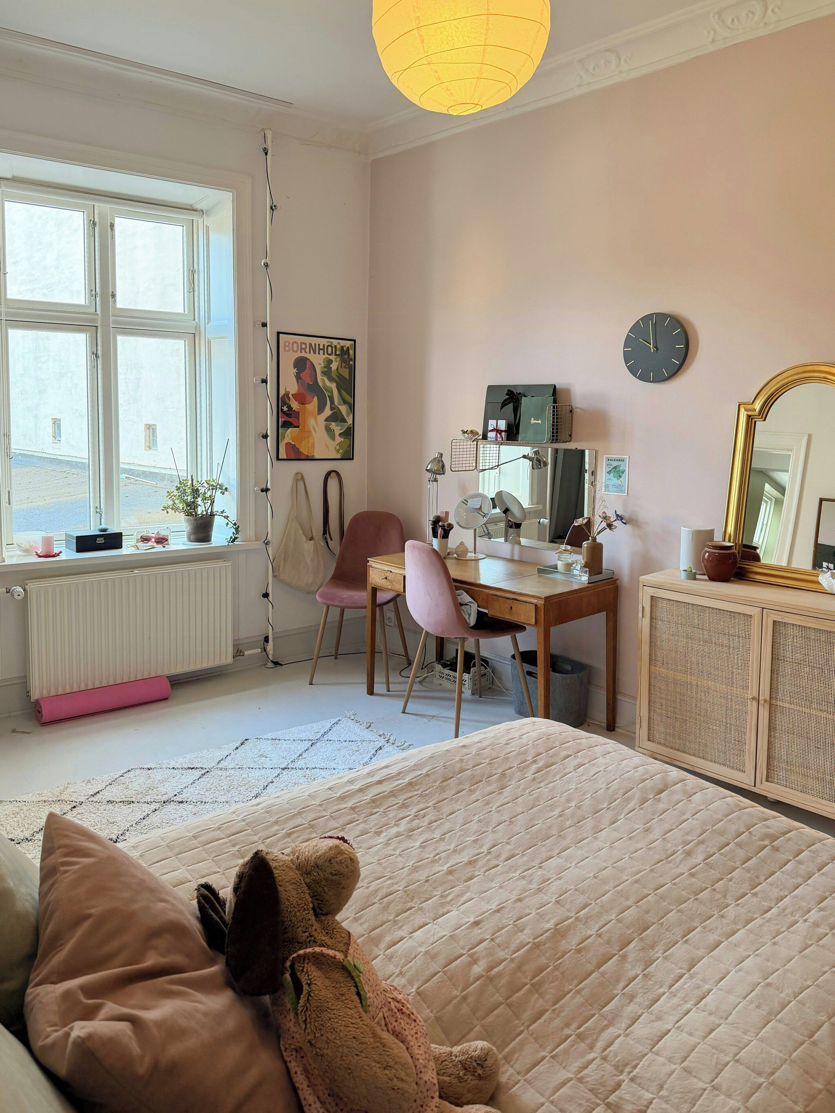 A bedroom with a bed, a desk, a chair, a radiator, a window, and a wall clock.