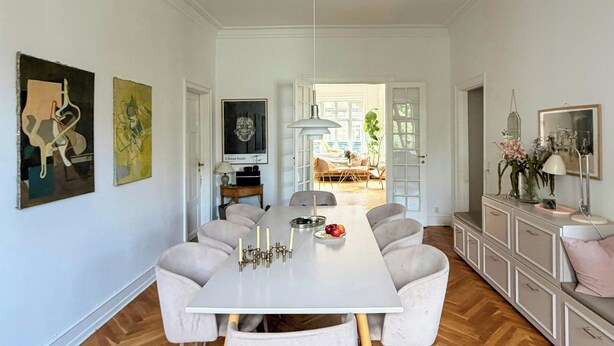Een ruime eethoek met een lange tafel, witte stoelen en een moderne hanglamp.
