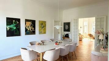 A spacious dining area with a large table and chairs, surrounded by white walls and wooden flooring.