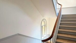 Een houten trap met houten leuning en witte balustrades, leidend naar een overloop met een witte muur en een raam.