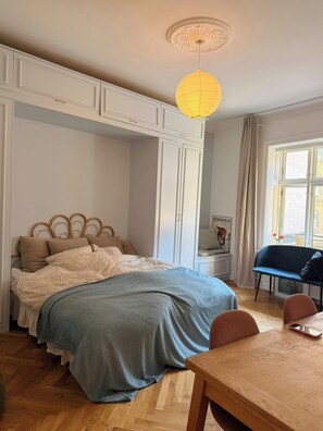 A bedroom with a bed, a wooden table, a chair, a desk, a lamp, and a window. - Historic flat from the 1850s in Frederiksberg (Frederiksberg)