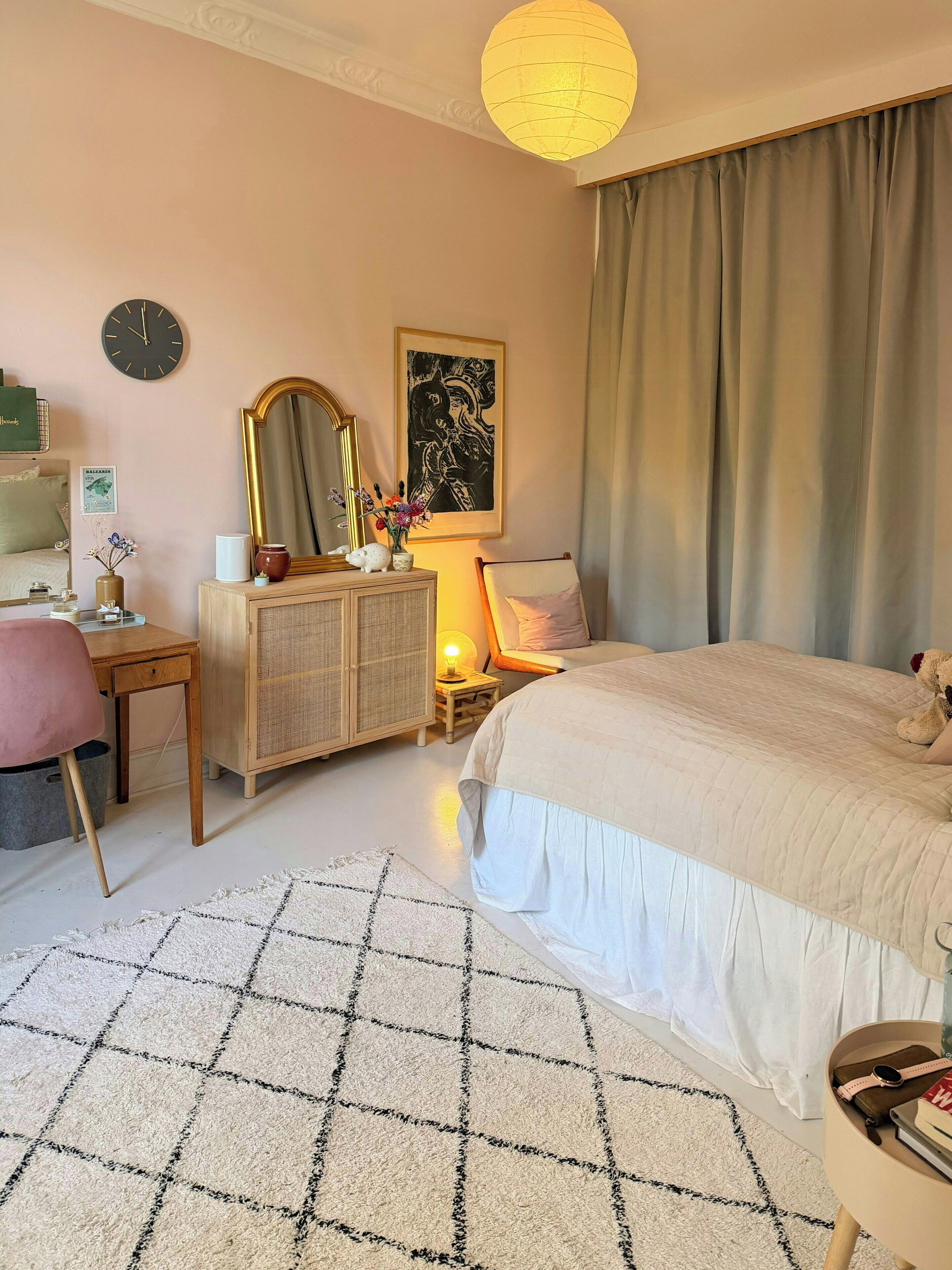 A bedroom with a bed, a desk, a dresser, a mirror, a clock, and a painting on the wall.