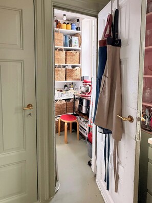 A narrow hallway leading to a kitchen area with shelves stocked with kitchenware and a stool.