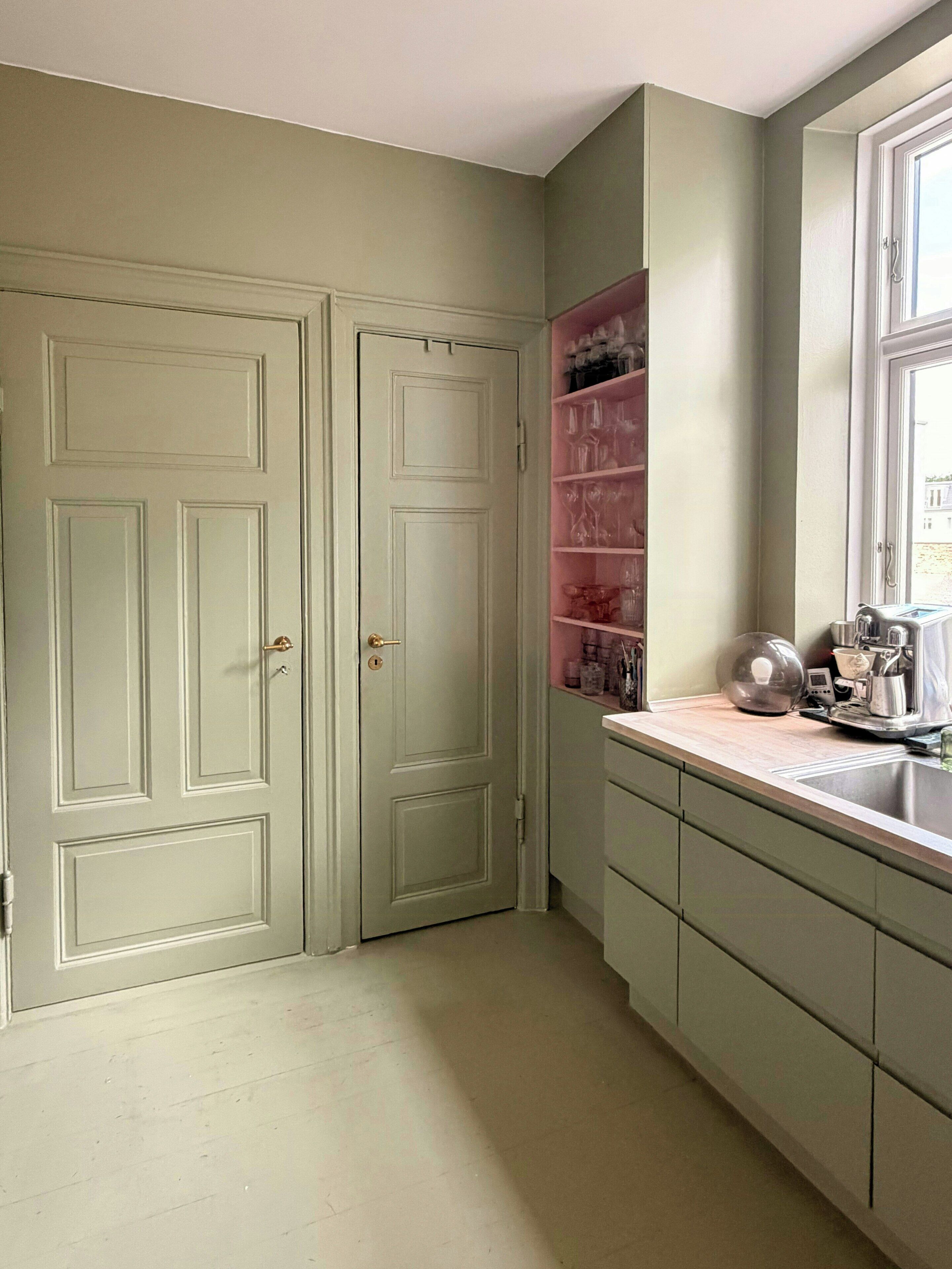 A kitchen with two double doors, a countertop with various kitchen items, and a window.