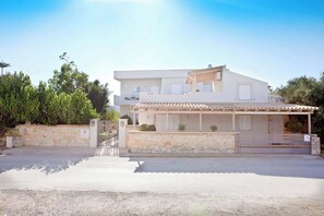 Una casa de dos pisos con un muro de piedra, entrada protegida por una reja y un porche cubierto.