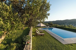Una piscina con solárium de piedra, rodeada de césped cuidado y un árbol grande.