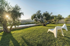 Un espacio al aire libre con césped, una piscina, sillas de plástico blanco y árboles.