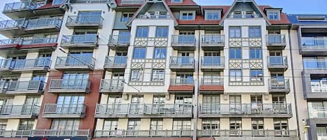 Un hôtel à plusieurs étages doté de balcons, d’une devanture de magasin et d’un espace de stationnement où les bagages peuvent être déposés.
