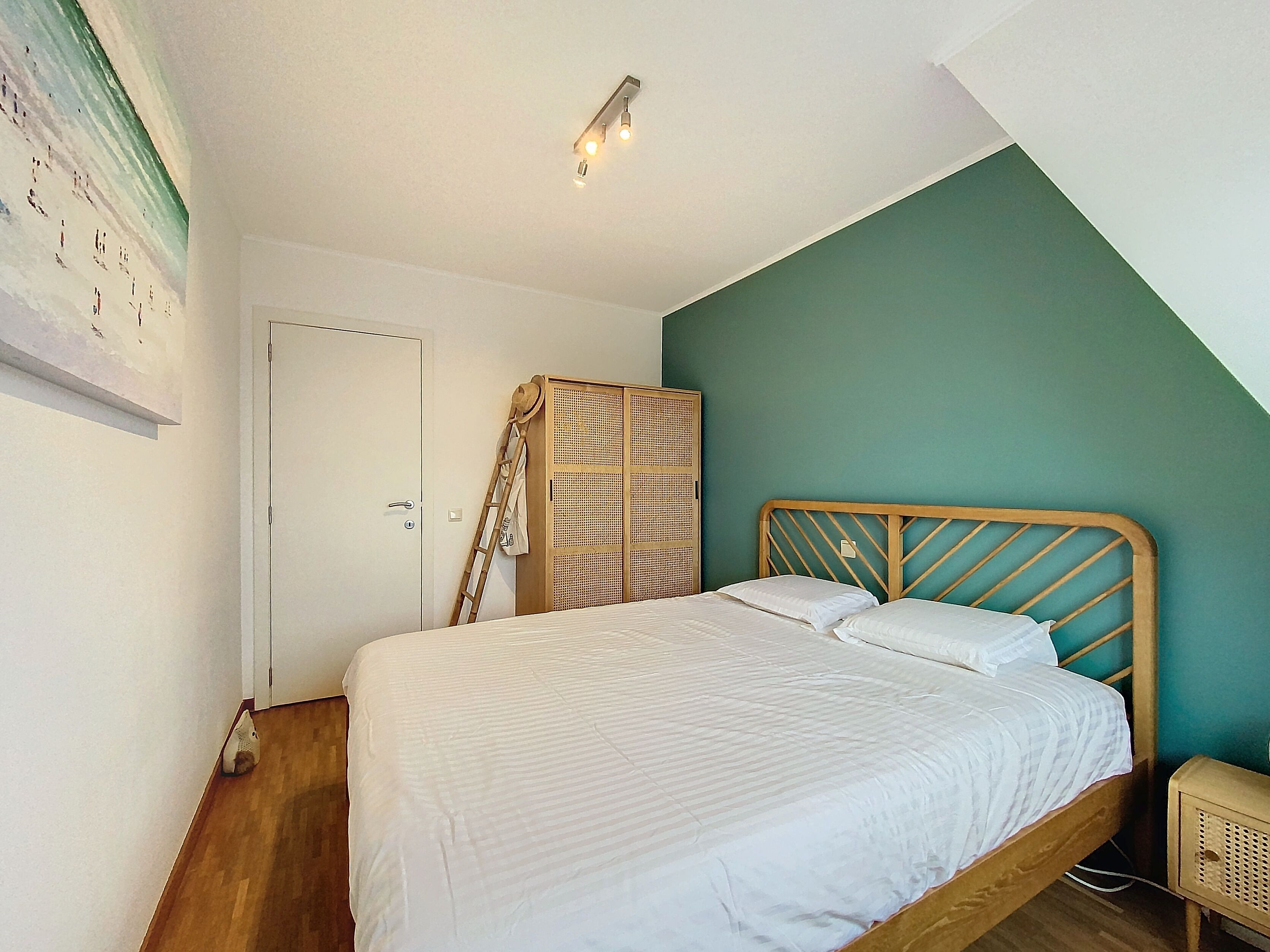 A bedroom with a bed, a wardrobe, a ladder, and a wall-mounted light fixture.