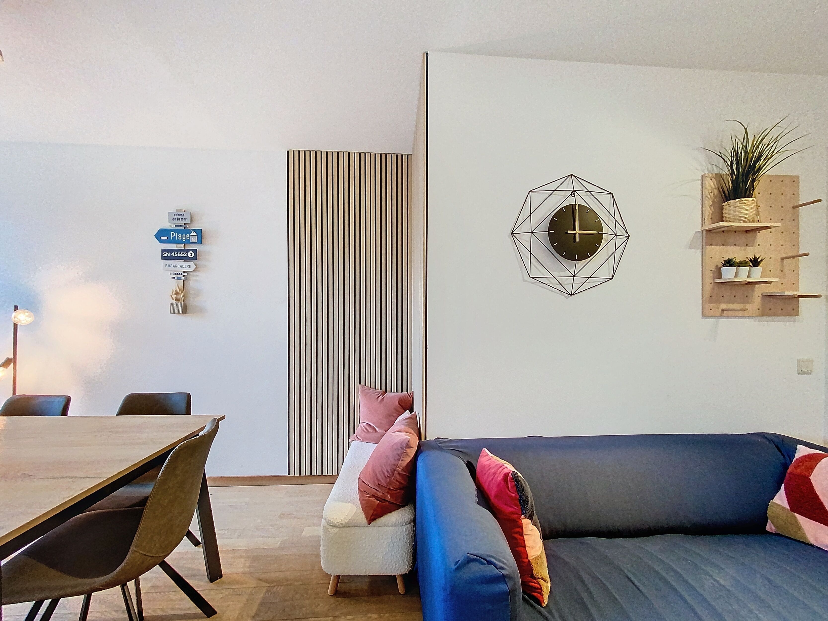 Een moderne woonkamer met een blauwe bank, een eettafel en een hangklok.