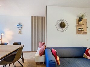 Ein modernes Wohnzimmer mit einem blauen Sofa, einem Esstisch und einer Wanduhr.