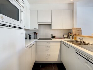 A modern kitchen with white cabinetry, a built-in microwave, a sink, and a coffee maker. - "Emmy" Apartment – Oostduinkerke – Cozy vacation apartment near the beach (Koksijde)
