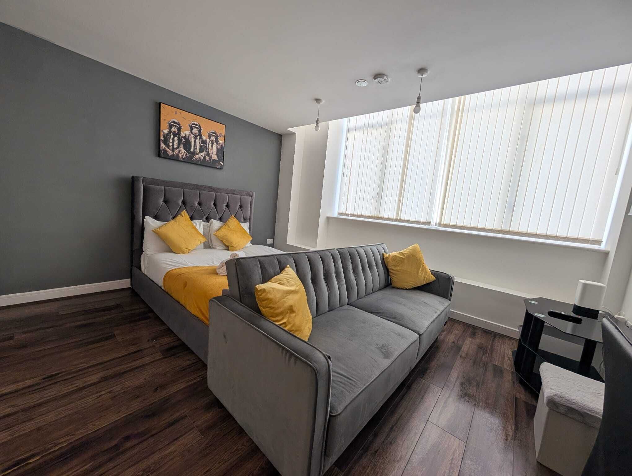 A modern bedroom with a bed, a gray sofa, and a large window with blinds.
