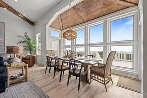 Ein Essbereich mit Holztisch und -stühlen, großen Fenstern und Blick ins Freie.
