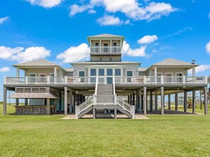 A beachfront property with a central staircase leading to a balcony, surrounded by a grassy lawn and a clear sky. - Where Family Beach Memories Begin: 3Bedrooms, 6 Bed Loft & Endless Gulf Views (Bolivar Peninsula)