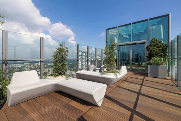 A rooftop terrace with modern seating, glass walls, and a city view.