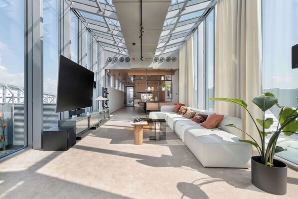 A modern living room with a large flat-screen TV, a sofa set, a coffee table, and a potted plant.