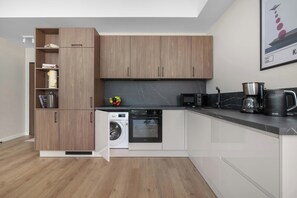 A modern kitchen with wooden cabinets, a built-in washing machine, a microwave, and a coffee maker.