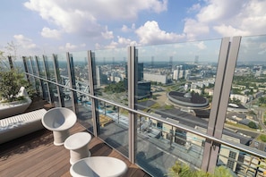 Een balkon op een hoog gebouw met een panoramisch uitzicht over de stad, voorzien van modern zitmeubilair en een glazen balustrade.