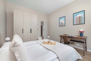 A modern bedroom with a bed, a desk, and two framed pictures on the wall.