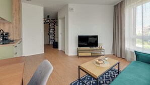 A modern living room with a television, a sofa, a coffee table, and a kitchen area with a stove. - Śląska 416 | Gym | AC & Parking (Gdańsk)