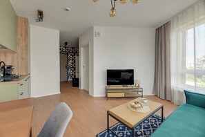 A modern living room with a television, a sofa, a coffee table, and a kitchen area with a stove. - Śląska 416 | Gym | AC & Parking (Gdańsk)