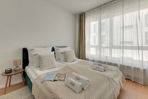 A neatly made bed with a textured blanket, a bedside table with a lamp, and a window with sheer curtains. - Śląska 406 | Gym | Perfect for Couples (Gdańsk)