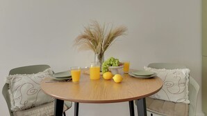 Una mesa redonda de madera con dos platos, dos vasos de zumo de naranja, un jarrón con plantas secas, un bol de uvas verdes y dos limones.