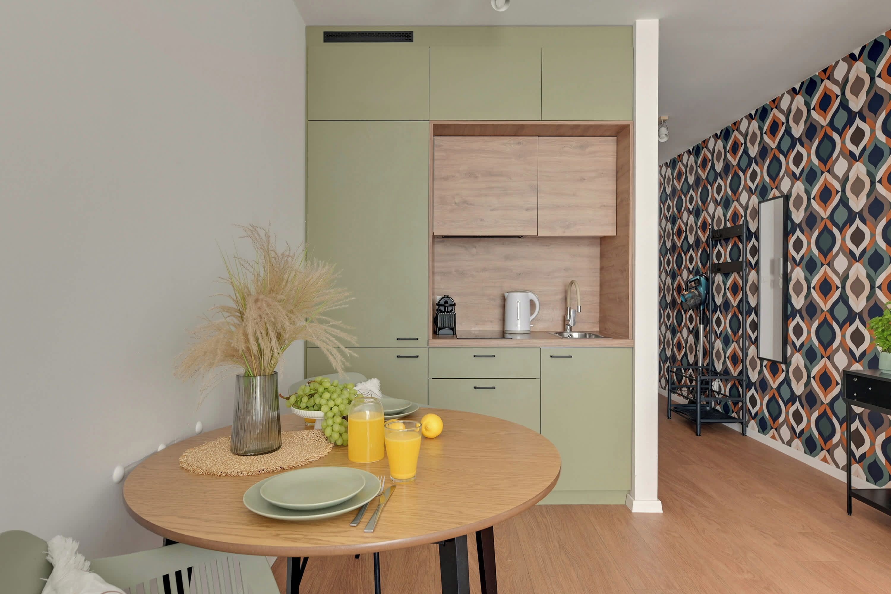 A compact kitchen with a dining area, featuring a round table with plates, cutlery, and a vase with dried plants.