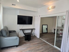 A living room with a grey sofa, a flat-screen TV mounted on the wall, a small black table, and a glass door leading to a kitchen. - Skytop ar Over The Rhine 6-bedroom 4 bath Cincinnati (Cincinnati)