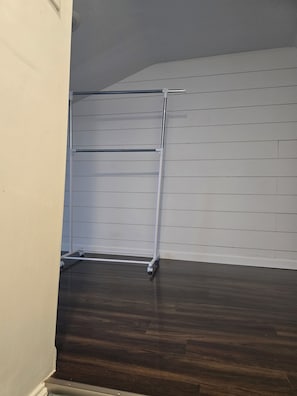 Una habitación con suelo de madera oscura, paredes blancas con paneles horizontales y un perchero de metal en la pared.