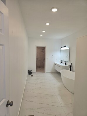 A modern bathroom with a large white bathtub, a vanity with a mirror, and a shower area. - Skytop ar Over The Rhine 6-bedroom 4 bath Cincinnati (Cincinnati)