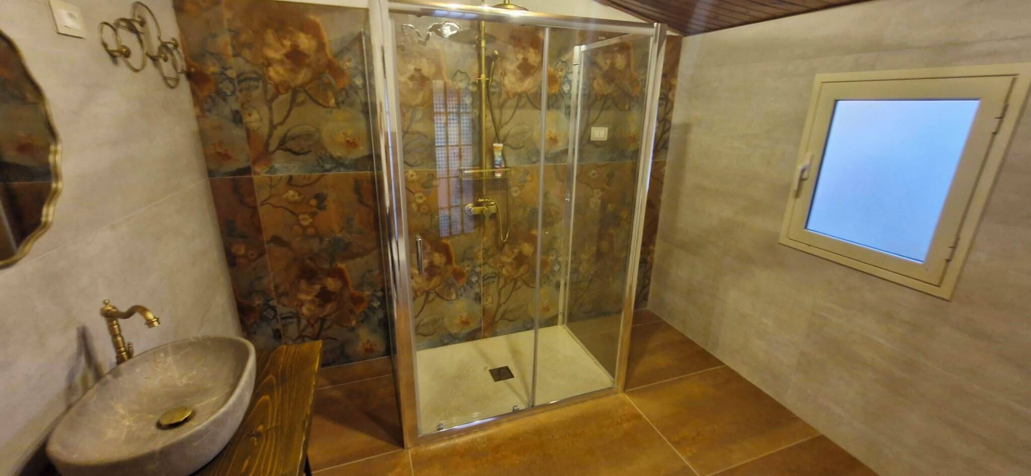 Un baño con cabina de ducha de vidrio, lavamanos y ventana.