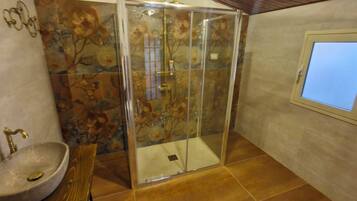 Un baño con cabina de ducha de vidrio, lavamanos y ventana.