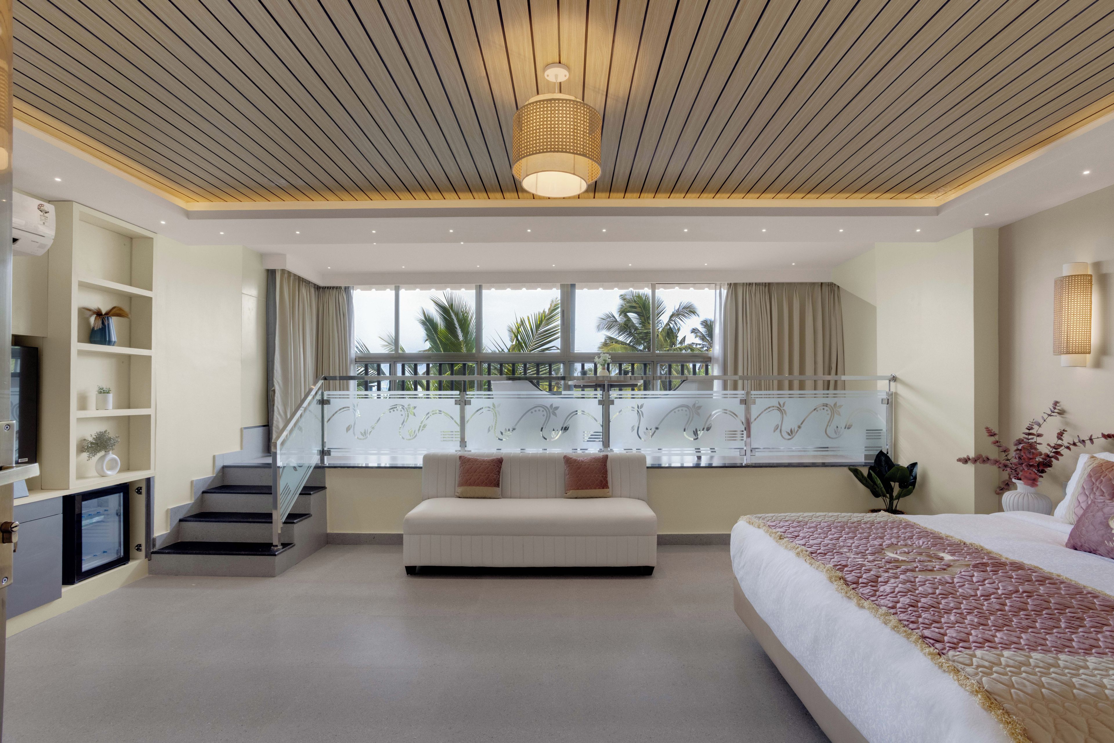 A modern bedroom with a large bed, a sofa, a TV, and a balcony with a railing.