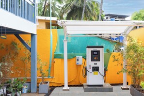 Una estación de servicio con bombas y un toldo blanco, ubicada en un espacio abierto con un muro amarillo y algo de vegetación.