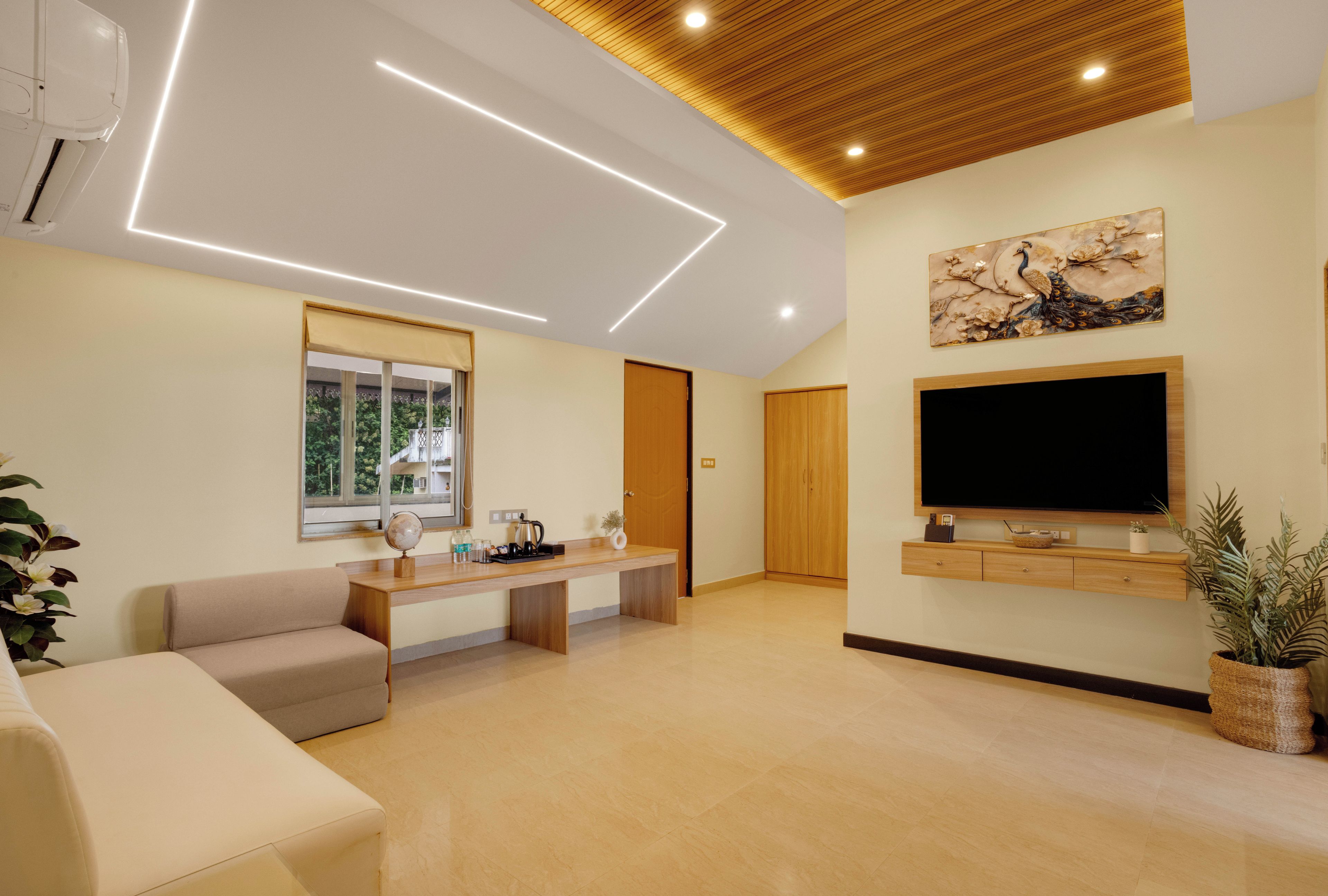 A modern living room with a flat-screen TV, a sofa, a coffee table, and a window with a view of greenery.